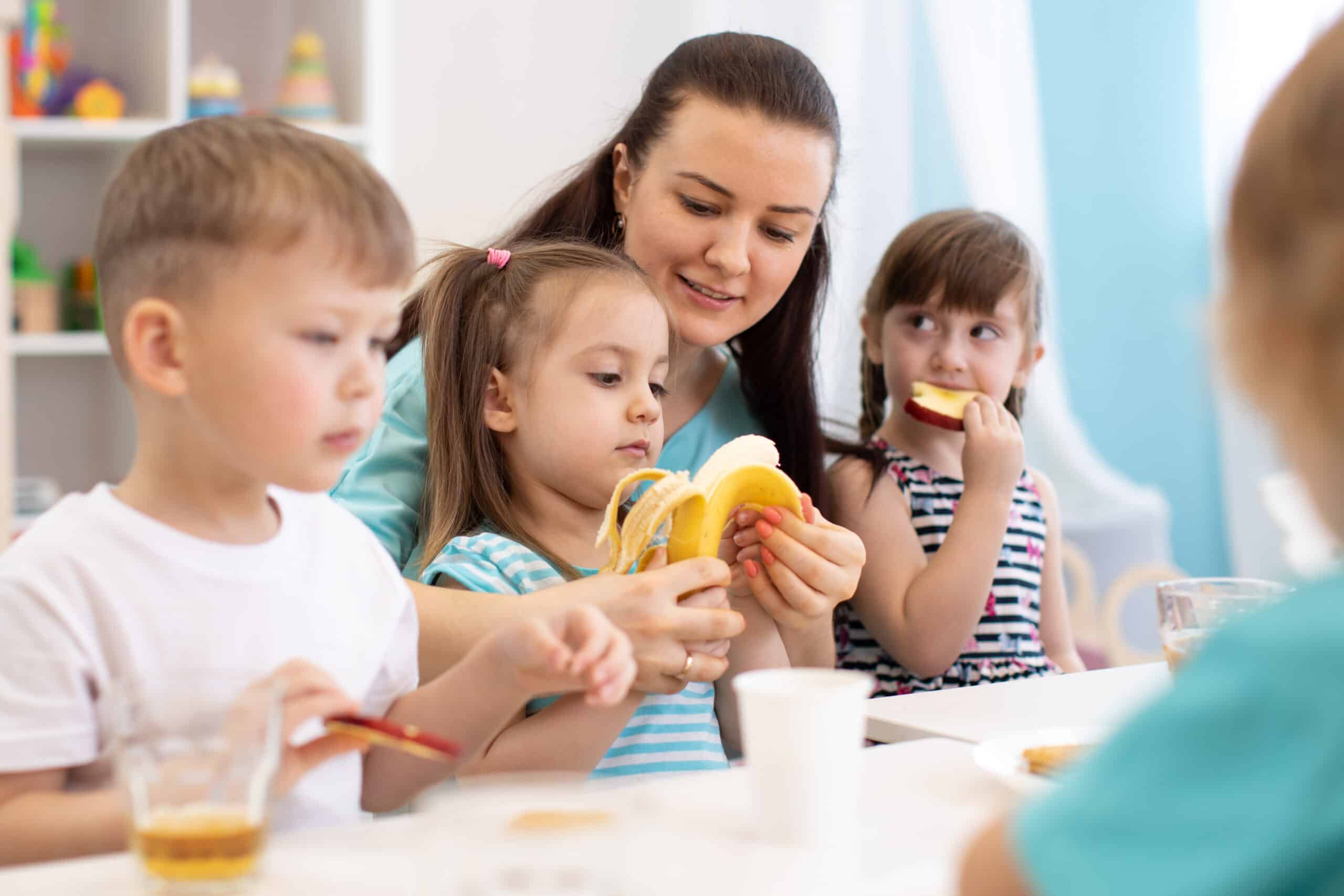 kindergarten teacher and preschoolers children having break for fruits and vegetables