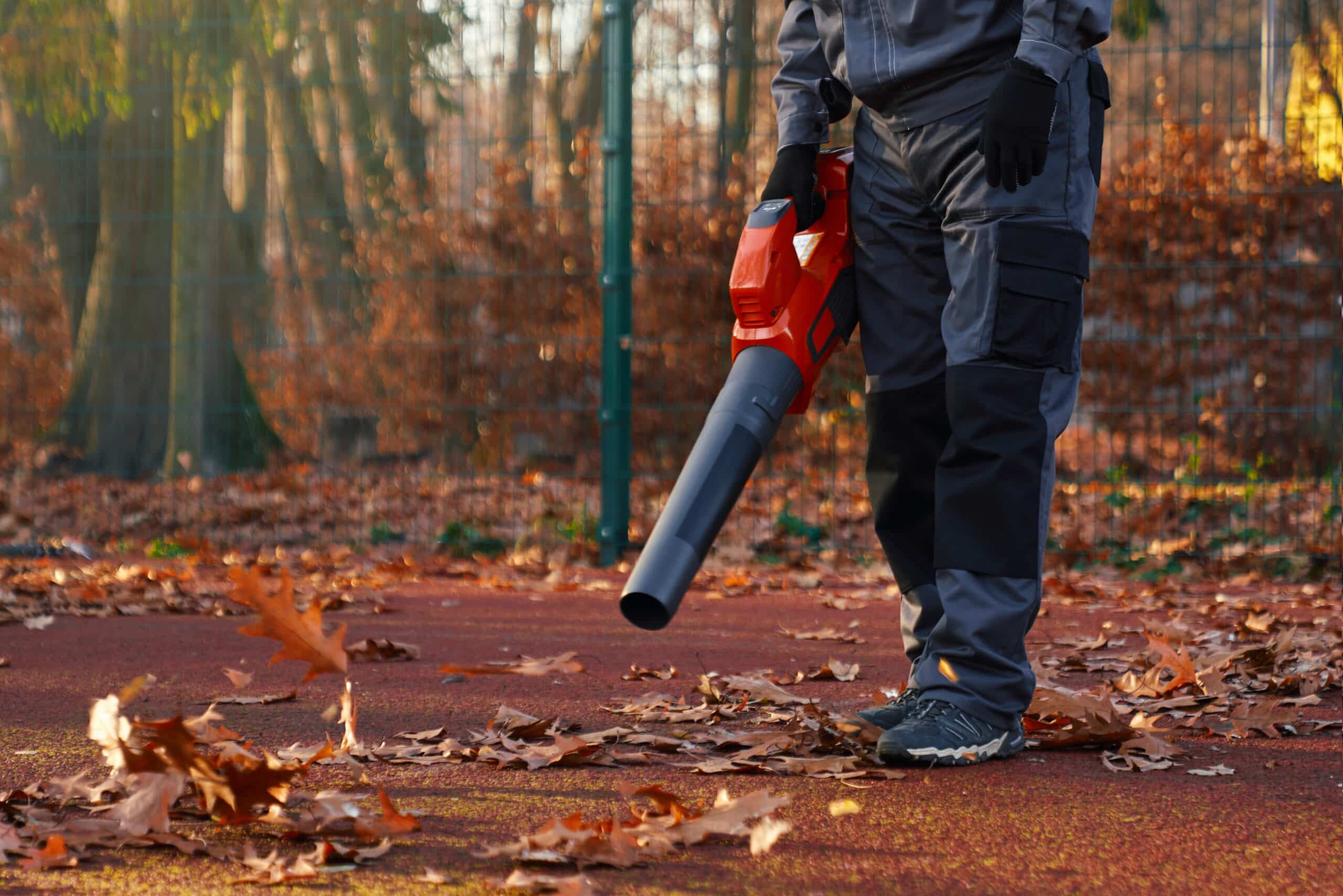 Male worker using leaf blower at park area.