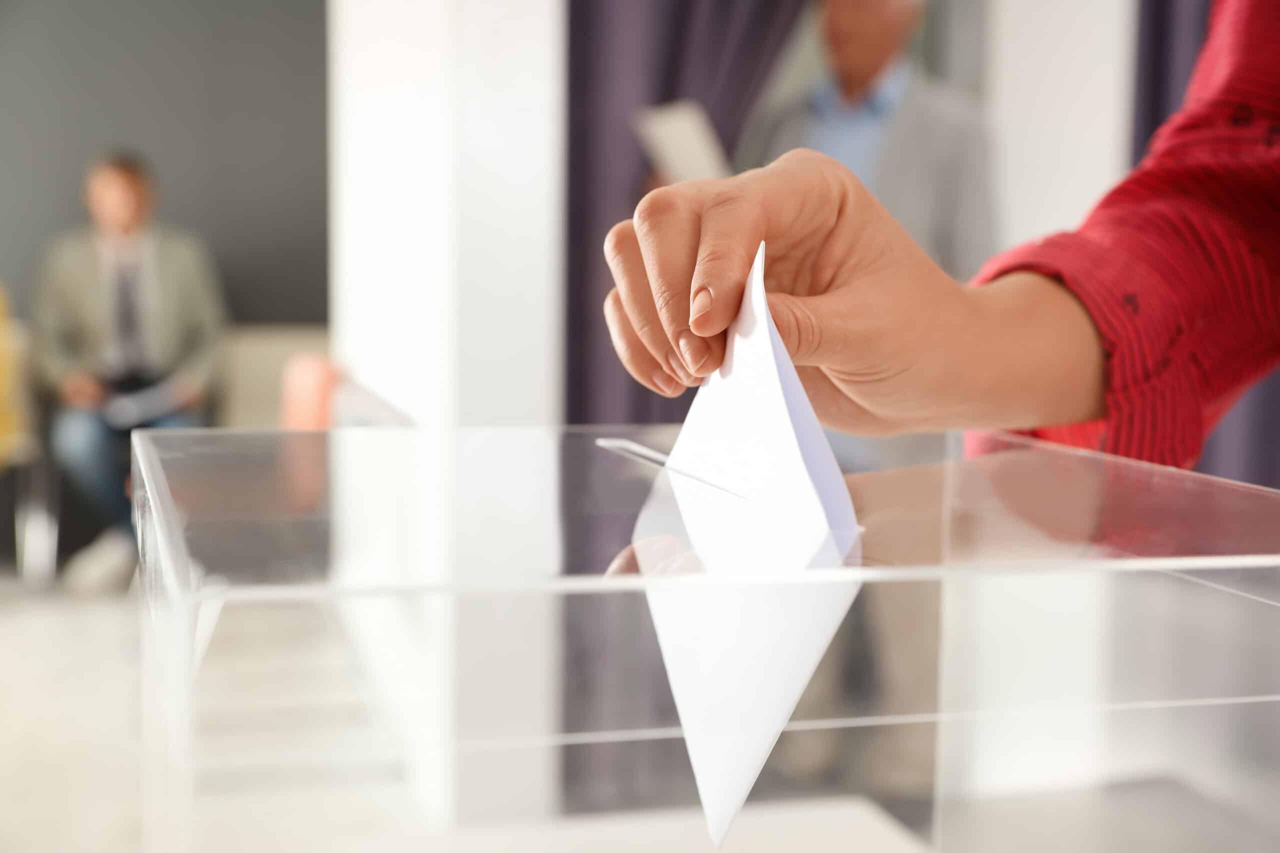 Woman putting ballot paper into box at polling station, closeup